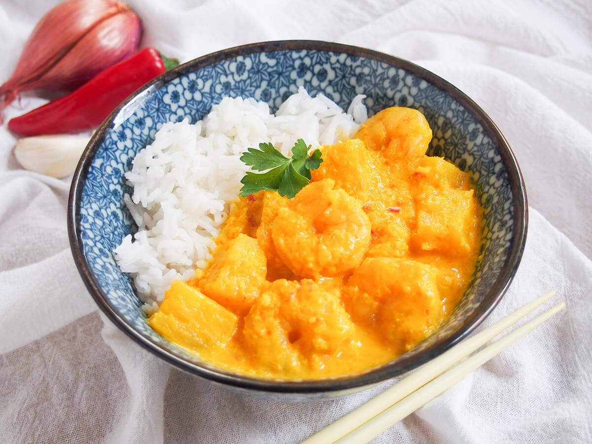 This pineapple shrimp curry is packed with sweet and spicy flavor. It's slightly adapted from a traditional Nyonya curry from Malaysia to be that bit quicker and easier, but just as delicious. bowl of pineapple shrimp curry with shallot and chili behind
