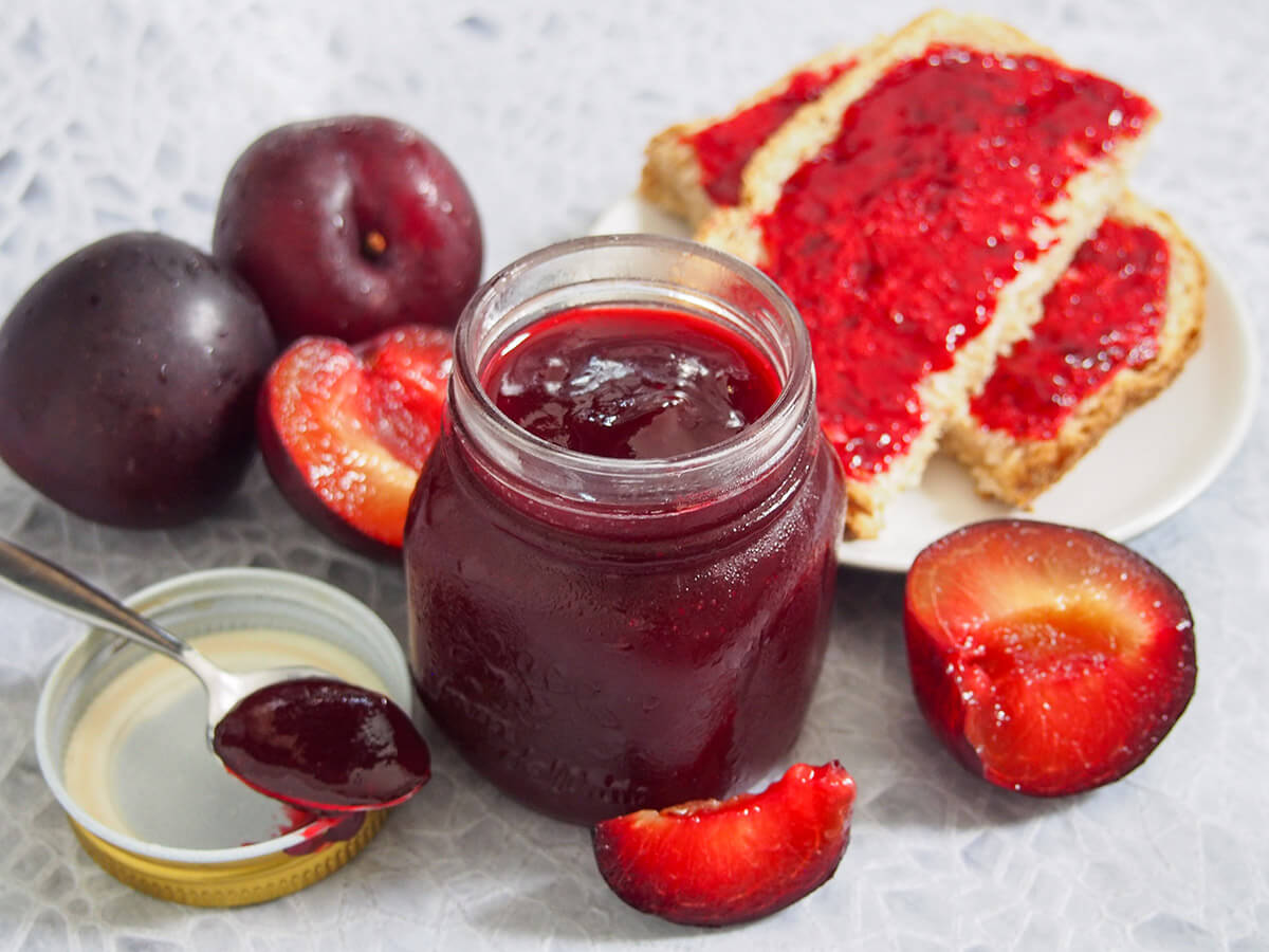 This easy plum jam has a wonderfully sweet and fruity flavor, with a touch of warm spice. It's lower on sugar but that lets the fruit flavor shine - no wonder it quickly became a family favorite. jar of plum jam with plums to side and bread with jam behind, spoon with jam to side of jar