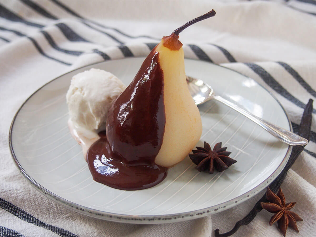 Poires belle Hélène might sound fancy, but these poached pears with chocolate sauce and ice cream are easy to make. Yet the result feels decadent, looks elegant and is all delicious. Perfect for entertaining or just because. plate of poached pears with chocolate sauce aka poire belle Helene with spoon behind pear