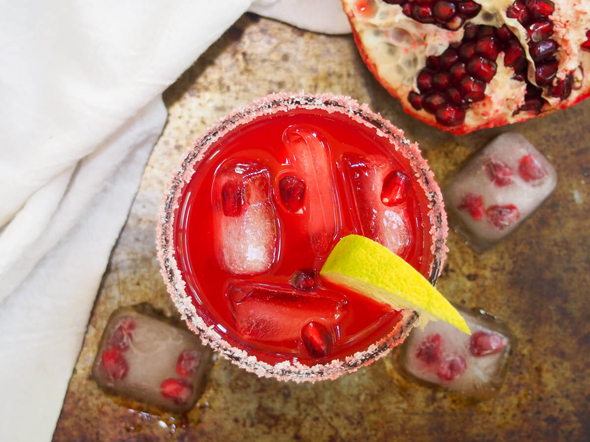 This pomegranate margarita is a bright and colorful twist on the classic cocktail. It has a wonderful balance of tart, fruity and sour flavors and is perfect for a festive occasion (or any excuse you want to make). glass of pomegranate margarita from overhead with pomegranate to side