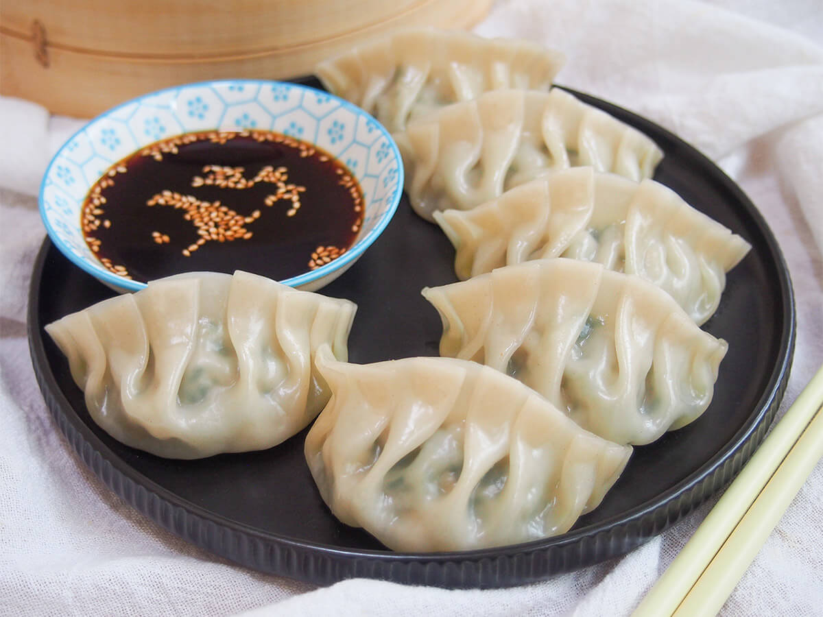 Pork and chive dumplings are a classic Chinese jiaozi - it's a simple, delicious combination balancing rich pork and bright herbs. Easy to make and so tasty. plate of pork and chive dumplings with dipping sauce to back of plate