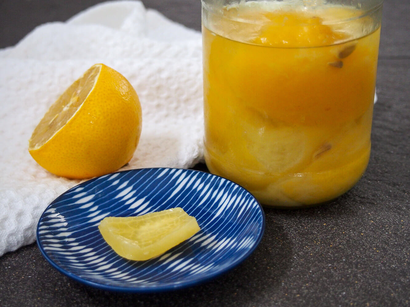 Preserved lemons are a common ingredient in Moroccan cooking, as well as other countries in the Mediterranean. They're so easy to make and add a wonderful salty-tart flavor and depth to a whole range of dishes from traditional tagines to salads. piece of preserved lemon in front of jar with more with fresh lemon half to side