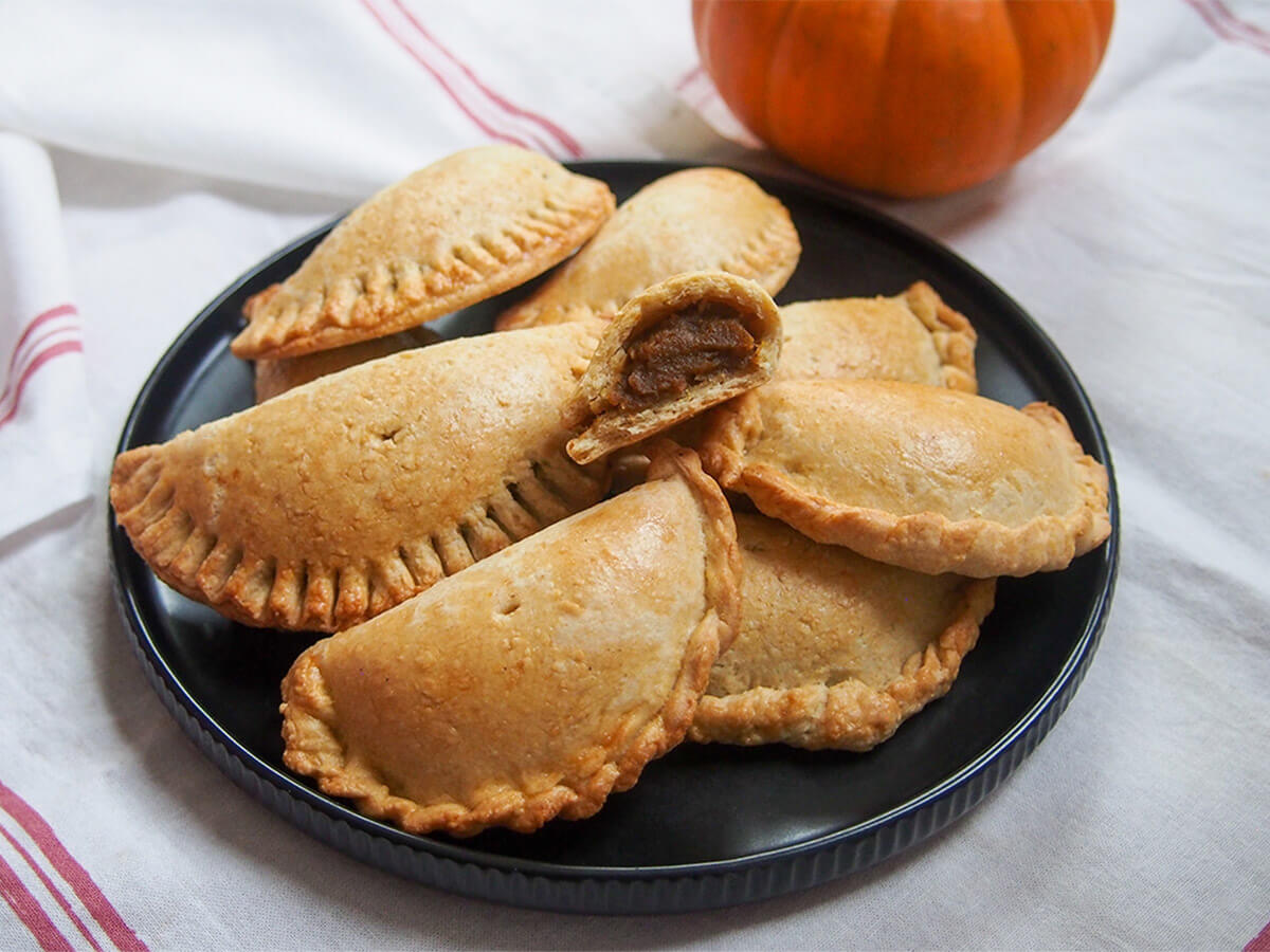 chocolate chip and pumpkin empanadas. Delicious pastry pockets with a smooth, soft spiced filling. Lower in sugar, part wholewheat, these are a healthier version too. plate of pumpkin empanadas with a broken one on top showing filling