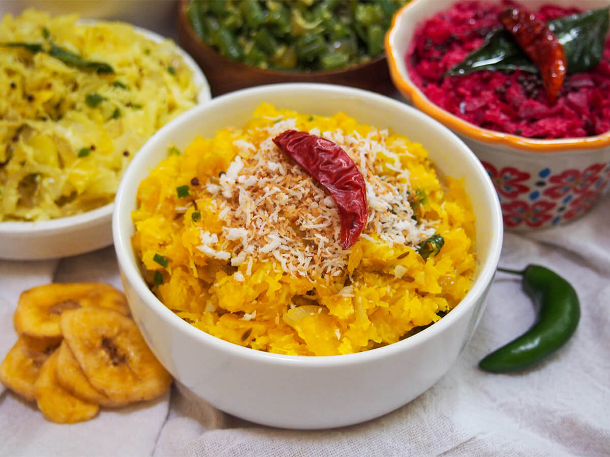 Pumpkin erissery is an easy and comforting Indian side dish with sweet, savory and spice flavors. It's mainly pumpkin and coconut along with relatively simple spicing and pairs perfectly with a range of other dishes. bowl of pumpkin erissery with bowls of thorans and pachadi behind