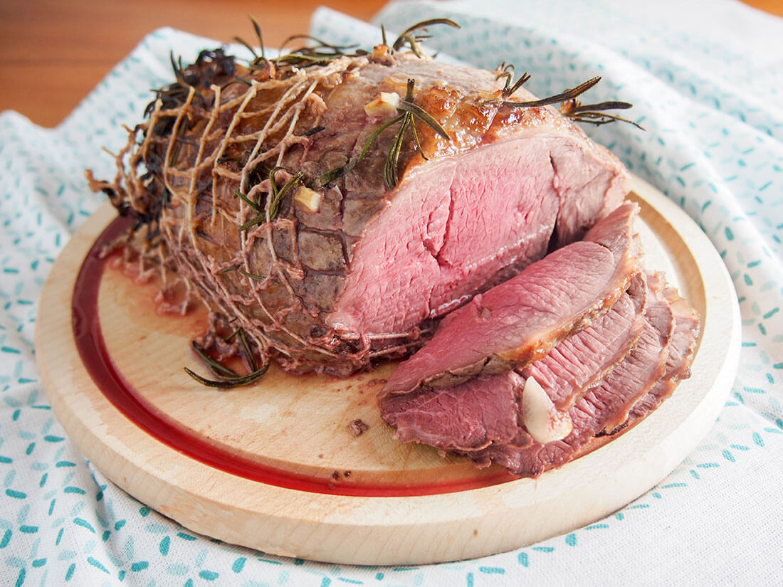 Roast lamb studded with garlic and rosemary and a simple lemon-honey-mustard glaze makes for a delicious center to an Easter meal, or enjoy any time. whole roast lamb on chopping board with slices to front