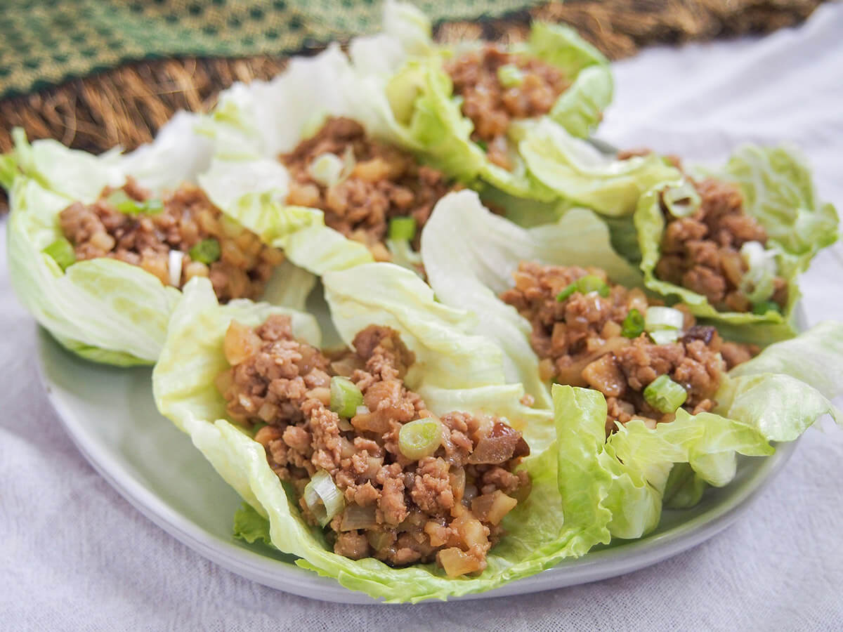 Whether you're looking for food to celebrate Chinese New Year, or just an easy low carb appetizer, these Chinese lettuce wraps are a delicious choice. (Plus the filling is great for meal prep!) plate of san choy bow Chinese lettuce cups with cloth behind plate