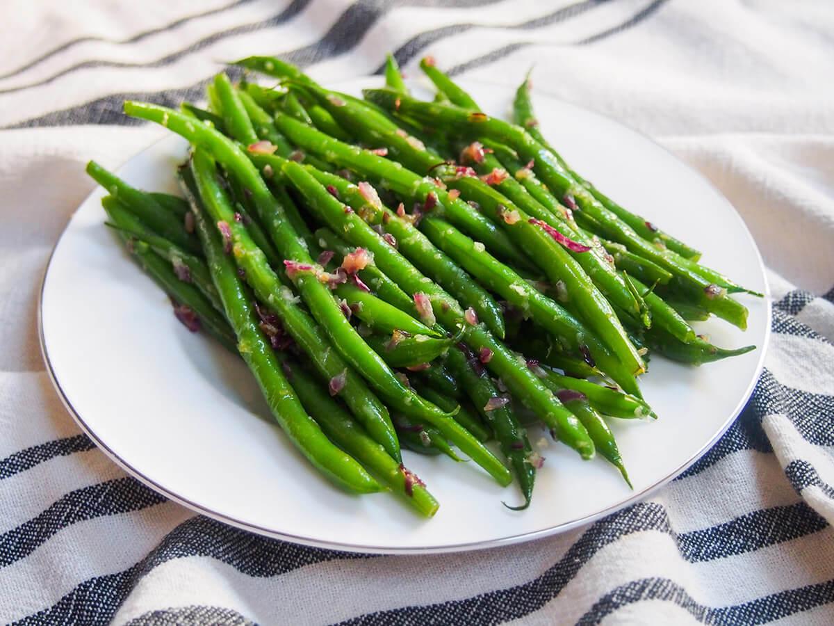 These sautéed French green beans are a wonderful way to dress up plain beans with wonderful flavor but minimal effort. The little touch of garlic and shallot pairs perfectly with the tender beans. They'll soon be a favorite side. plate of sautéed French green beans