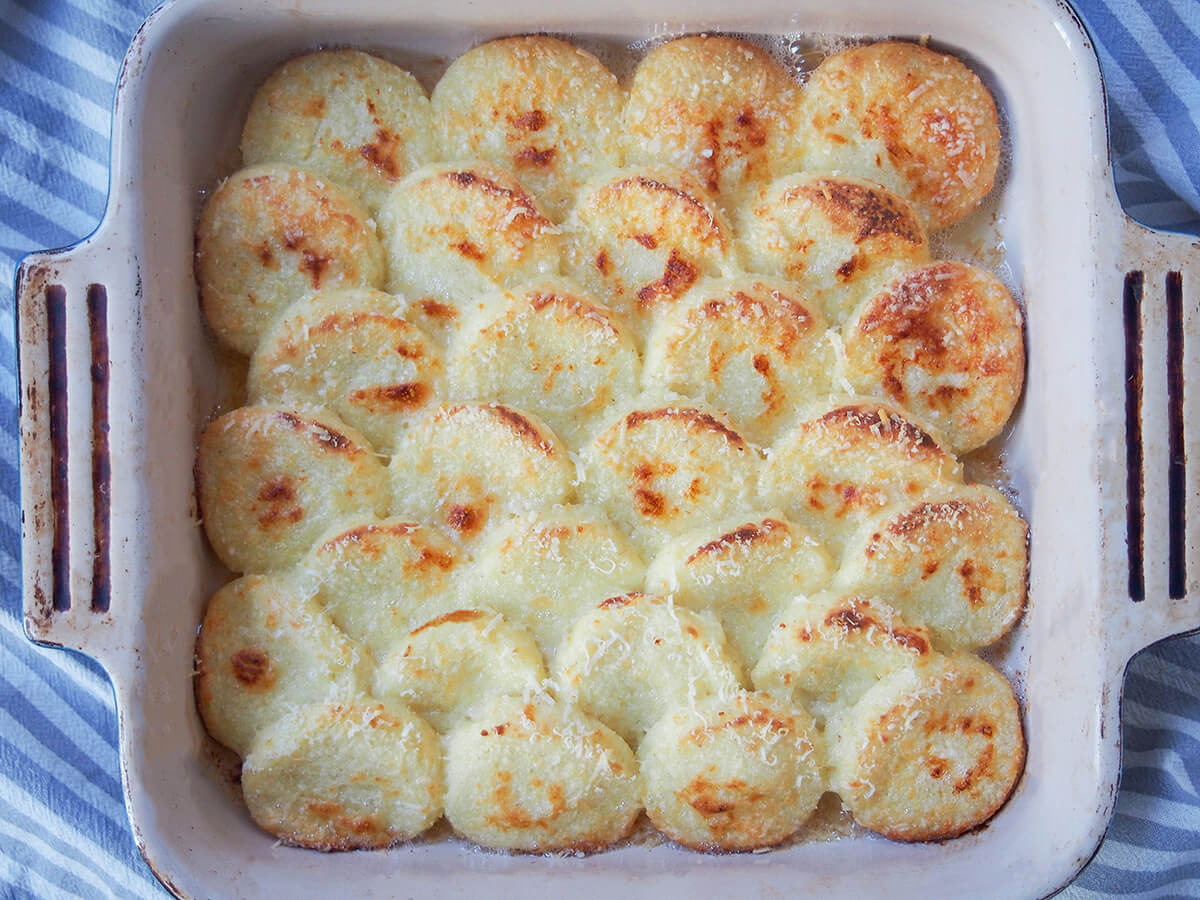 Gnocchi alla Romana (semolina gnocchi) dish of semolina gnocchi, gnocchi alla Romana, from overhead with handles of dish showing either side.