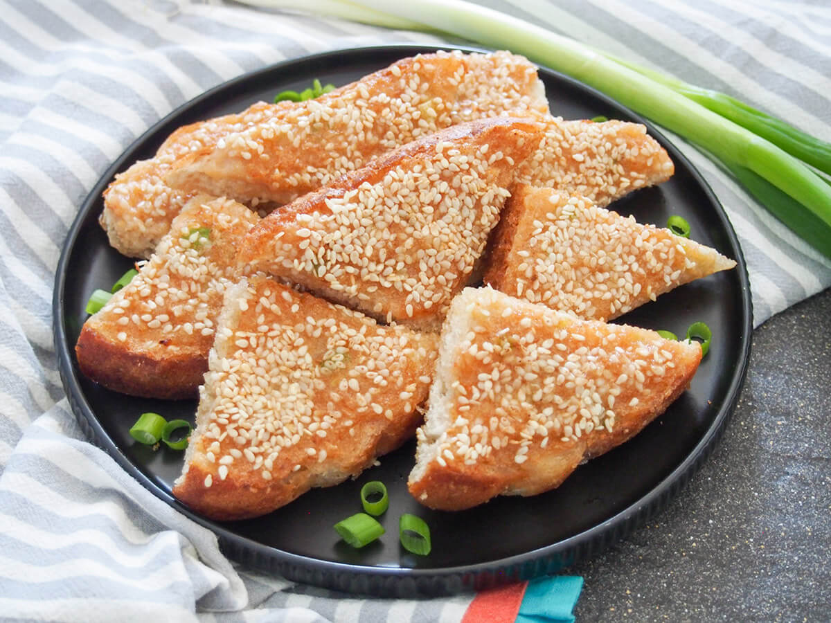 Sesame shrimp toast (prawn toast) is a Chinese takeout favorite that's easy to recreate at home. It's crisp, packed with flavor and makes an addictively good appetizer or snack. plate of sesame shrimp toast with spring onion behind