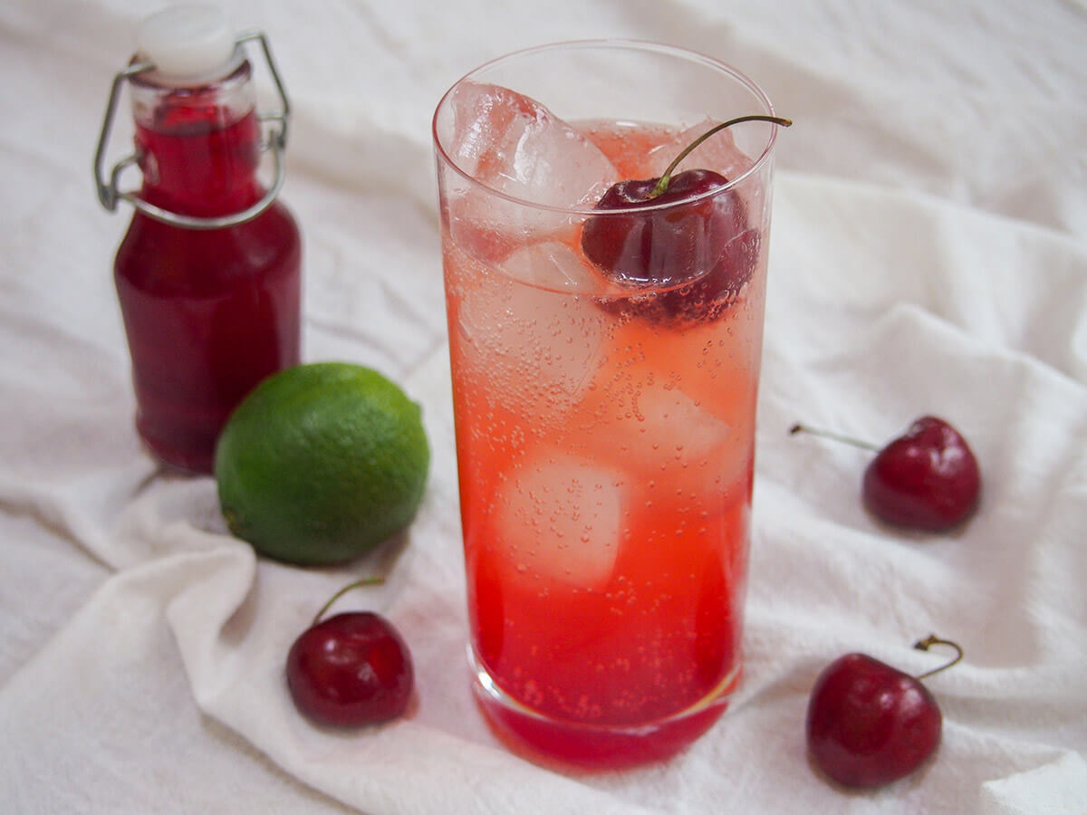 The Shirley Temple drink is a super simple family friendly combination. It has bubbles, a little sweetness and tartness and is a wonderful bright color - perfect to please kids and adults alike! glass of Shirley Temple drink with lime and bottle of grenadine behind