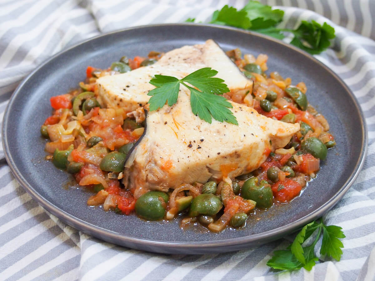 This Sicilian swordfish with olives and capers is a deliciously bright combination of tender fish in a tomato-based sauce. The slightly briny flavors of the olives and capers contrast with the sweeter onion and tomatoes. And what's more, it's so easy to make plate of Sicilian swordfish with olives and capers