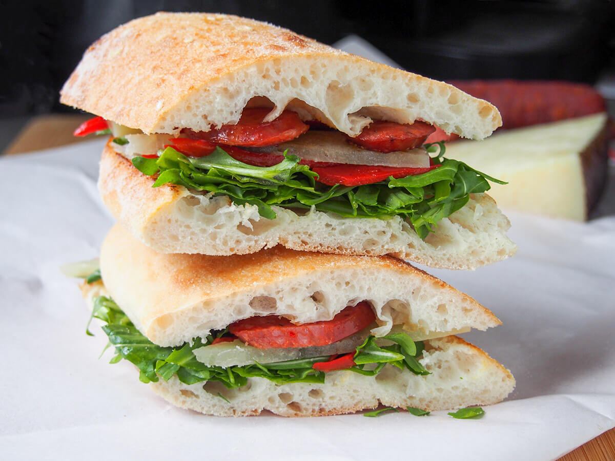 This tasty Spanish chorizo sandwich is packed with bright colors and flavors, with arugula, piquillo peppers and manchego cheese. It's quick to make and thoroughly delicious. A perfect quick lunch! two halves of Spanish chorizo sandwich stacked on top of each other