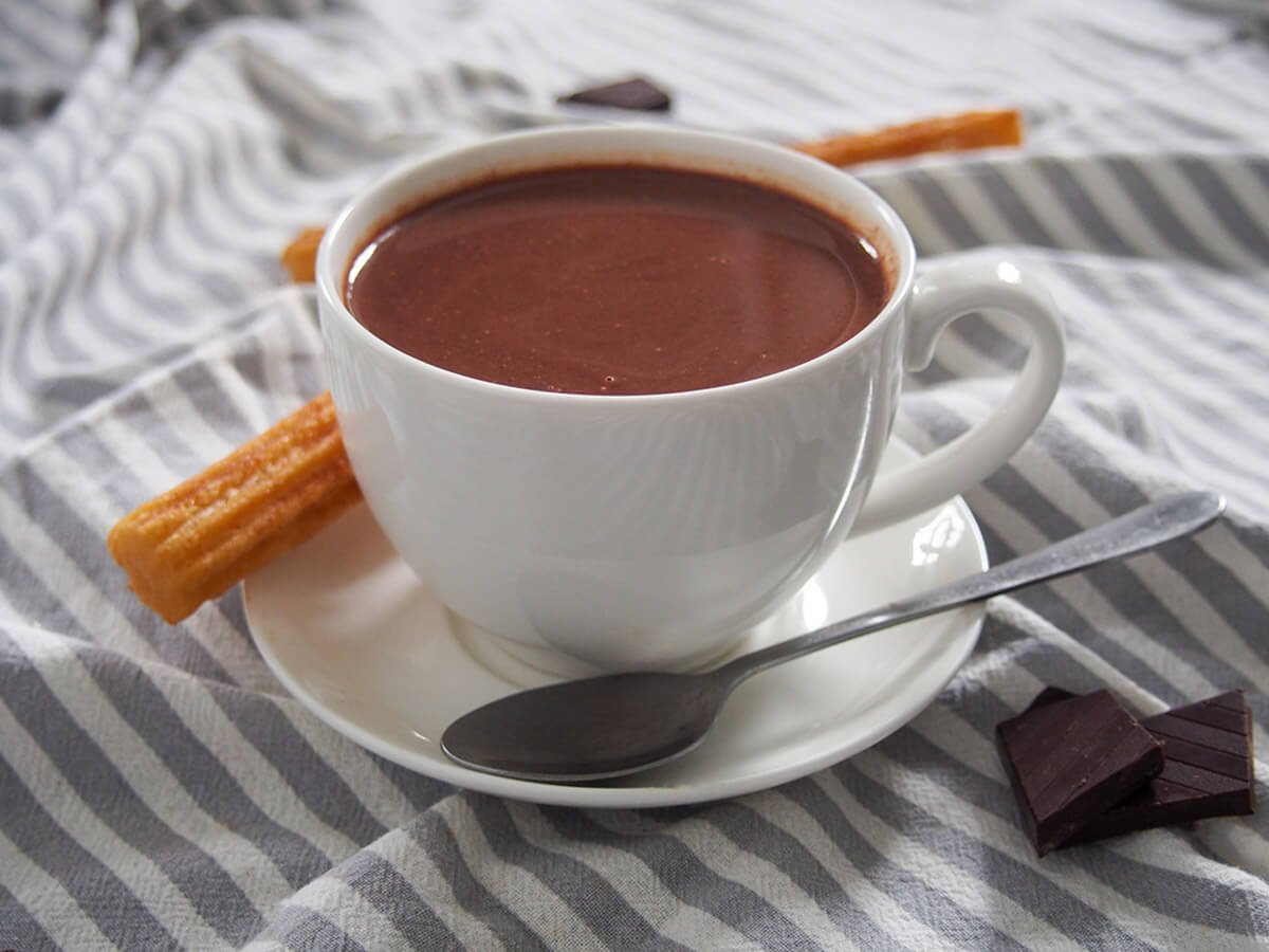 Spanish hot chocolate, 'chocolate caliente', is a wonderfully thick, rich and delicious treat. It's the traditional partner to freshly made churros, but it's also perfect just on it's own, especially on a cold day. cup of Spanish hot chocolate with spoon in front and churro behind