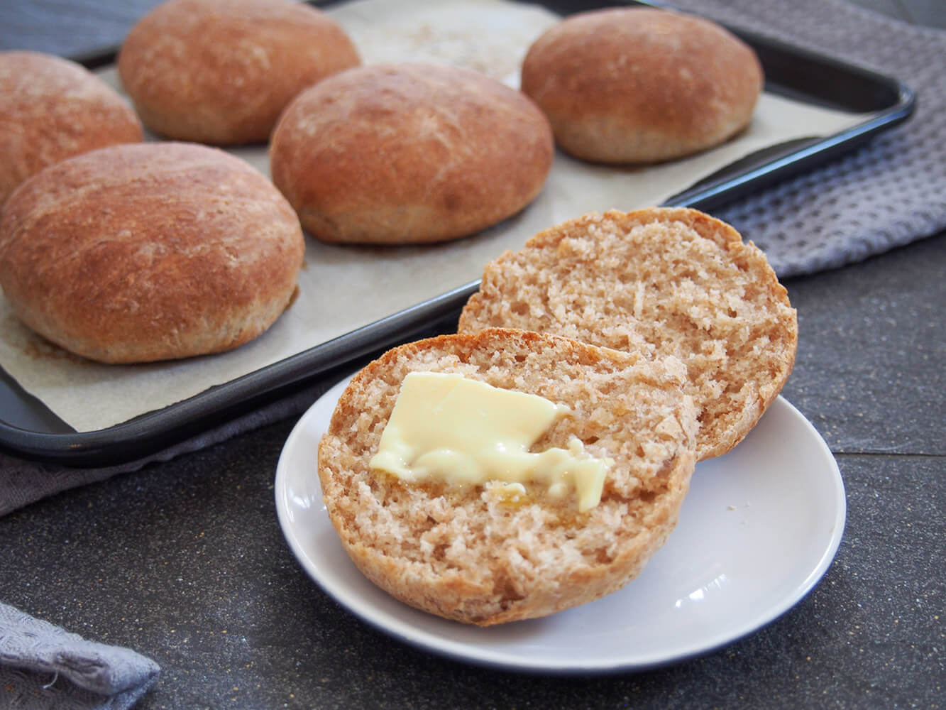 These spelt rolls have a wonderful lightly nutty flavor, tender crumb and are perfect for lunch or as a side to a meal. Soft, flavorful and versatile. finished bread roll with butter on top and other rolls behind