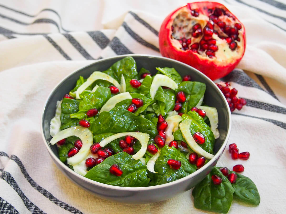 Super simple, highly adaptable and festively colored, this spinach pomegranate salad makes a great side or appetizer. It takes no time to make, and you'll love the bright, fresh flavors. side view of bowl of spinach pomegranate salad with pomegranate behind