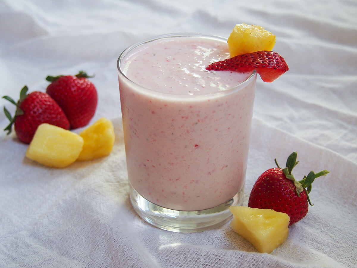 This super simple, four ingredient strawberry pineapple smoothie is light, fruity and refreshing. It works perfectly as part of breakfast, snack or after a workout. glass of strawberry pineapple smoothie with fruit to side