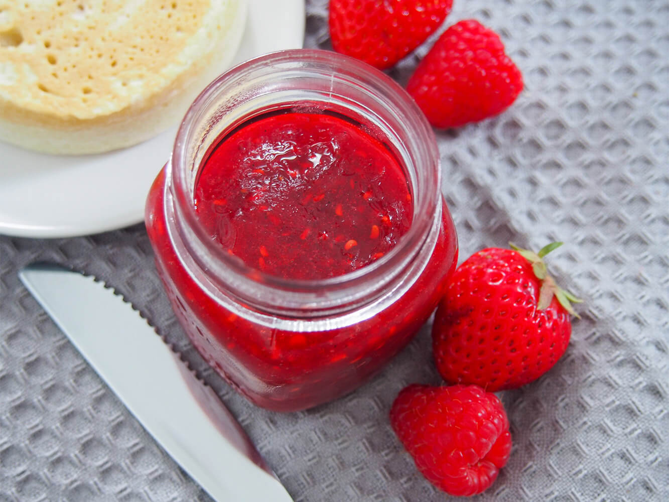This strawberry raspberry jam is a delicious combination of summer berries in a sweet, bright spread. This recipe makes a small batch in no time that's perfect to top your toast and more. strawberry raspberry jam in jar from overhead with fruit to side and crumpet on plate in corner