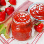 jar of strawberry rhubarb jam with rhubarb and strawberries behind
