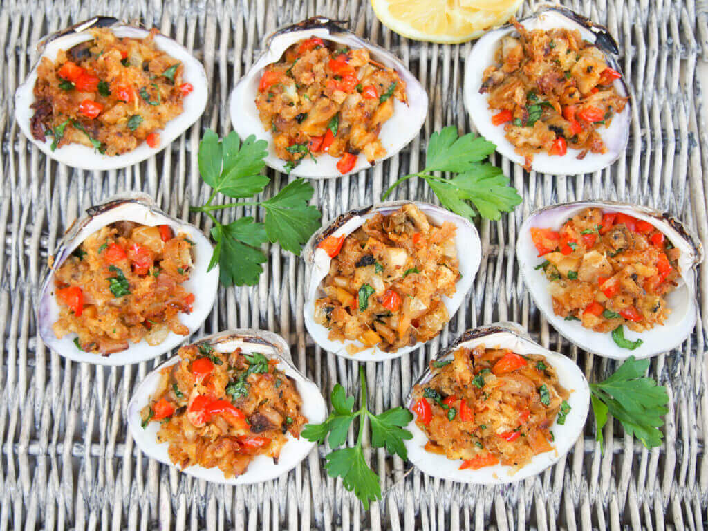 New England style stuffed clams are a delicious appetizer made with steamed clams & seasoned buttered breadcrumbs, baked until crisp on top but moist inside. New England-style stuffed clams on basket with parsley garnish between clams