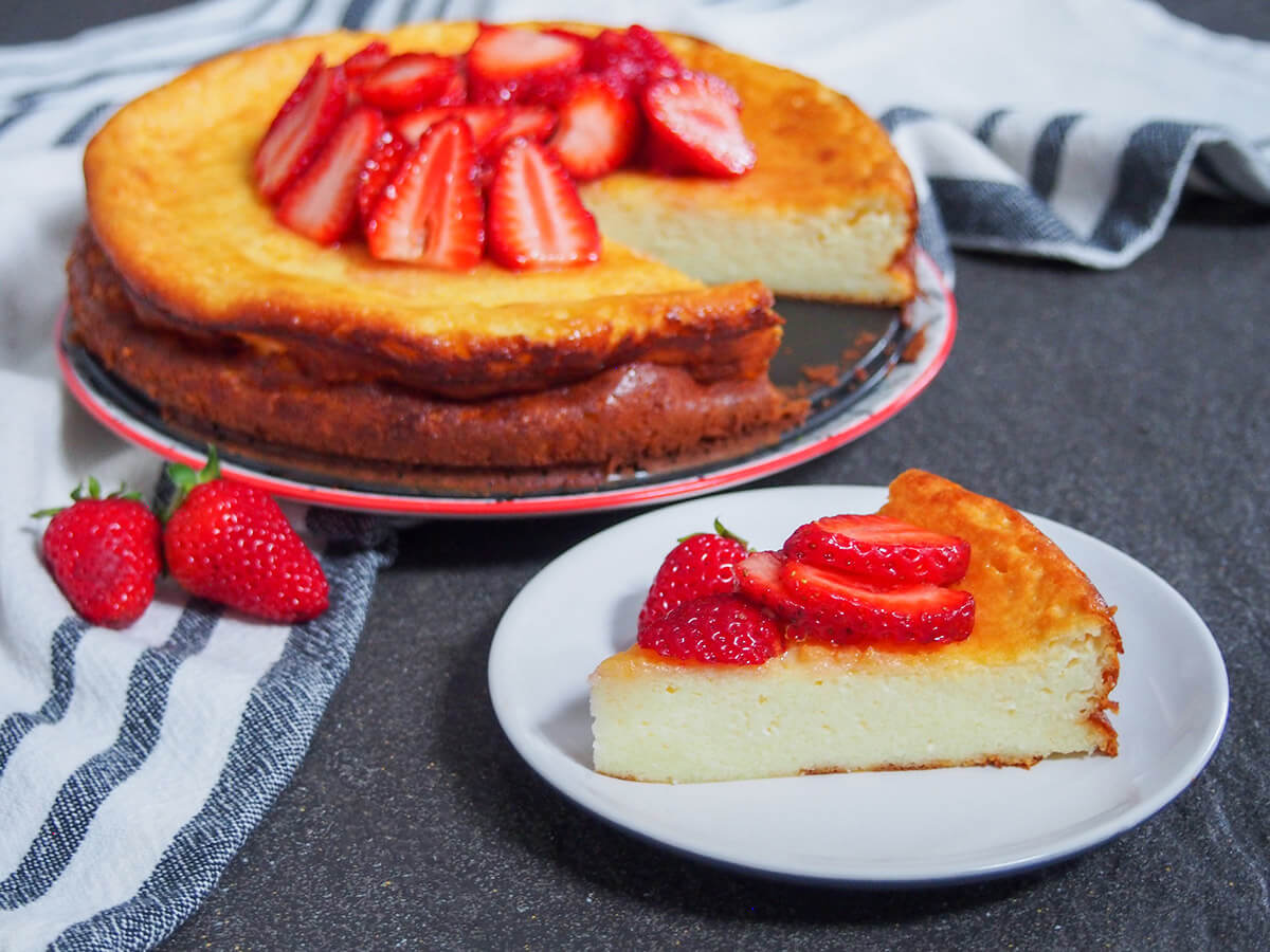 This Swedish cheesecake with strawberries (ostkaka), is made with cottage cheese and almonds. While not as sweet as an American cheesecake, it's equally delicious. plate with slice of Swedish cheesecake in front of rest of cheesecake