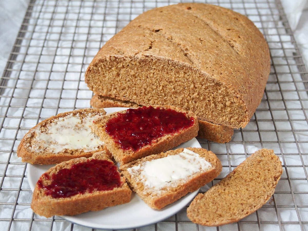 part loaf of Swedish limpa bread with some slices with butter and jam plate with slices of bread topped alternately with butter and jam and rest of Swedish limpa bread loaf behind.