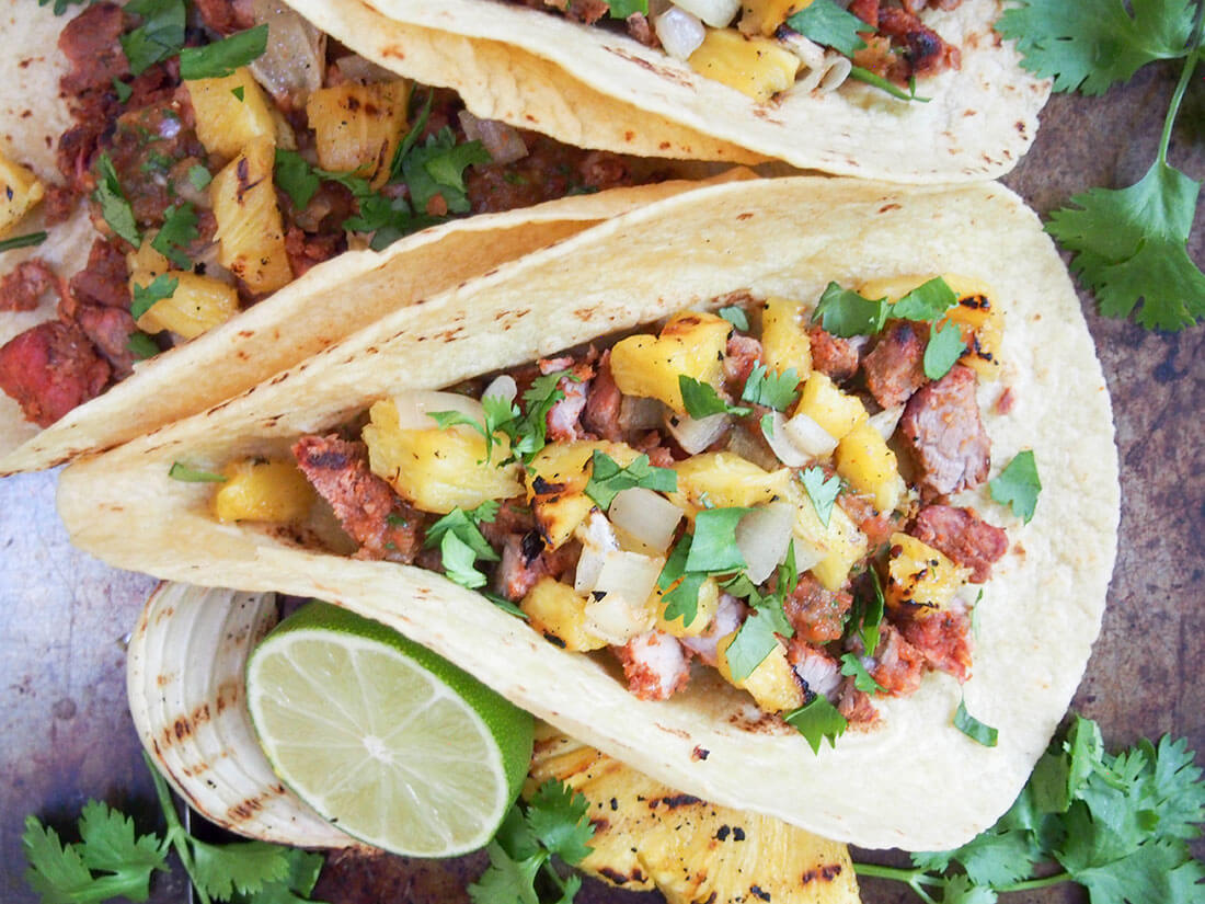 Tacos al pastor are traditionally cooked on a spit, but you can cheat a little and get all the same delicious flavor on your grill. Then wrap all the sweet-spiced pork and pineapple in a tortilla and enjoy! tacos al pastor topped with pineapple