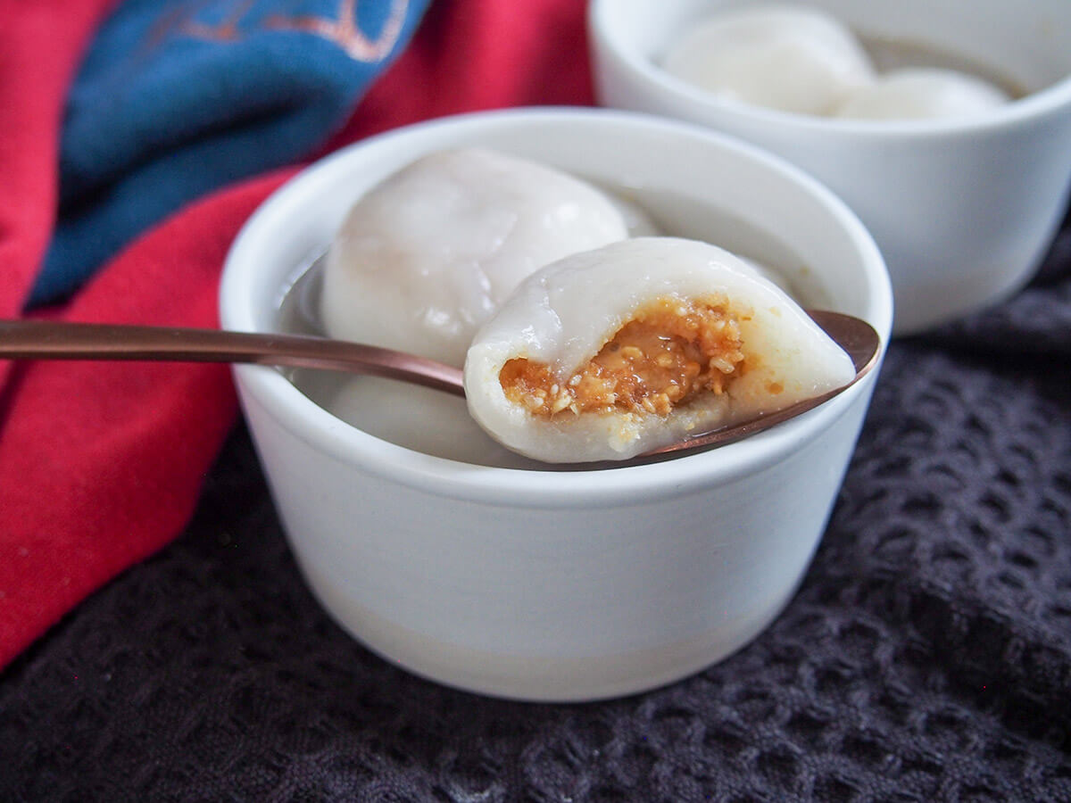 These Chinese sweet dumplings, tangyuan, are filled with a peanut mixture that's a wonderful contrast to the slightly gooey outside. They are traditionally served for the lantern festival but delicious enough to enjoy any time. peanut filling showing on Chinese sweet dumplings - tangyuan - resting on bowl with more