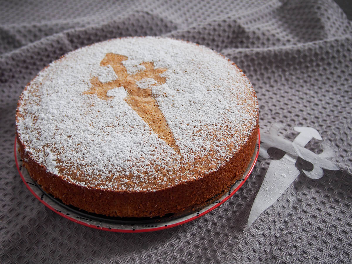 Tarta de Santiago is an almond cake from Spain that couldn't be easier to make. It's naturally gluten free, with a little brightness from lemon and lovely sweet, soft texture. Great for coffee time or dessert. tarta de Santiago almond cake from side with stencil to side of plate