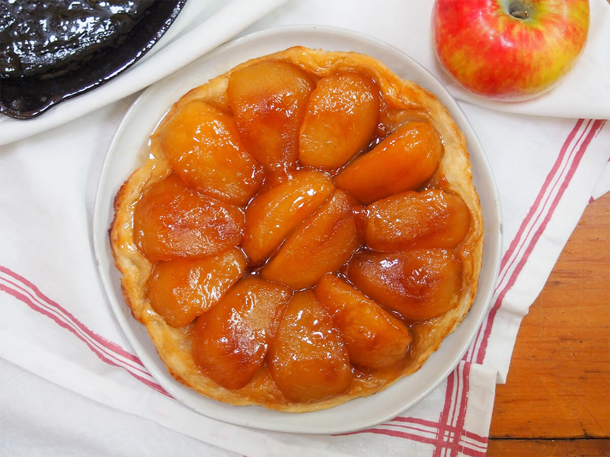 Apple tarte tatin is a classic French dessert that tastes wonderfully indulgent, despite only a few ingredients. An upside down tart with luscious caramel-coated, tender apples and is oh so good. apple tarte tatin from overhead with part of whole apple showing above