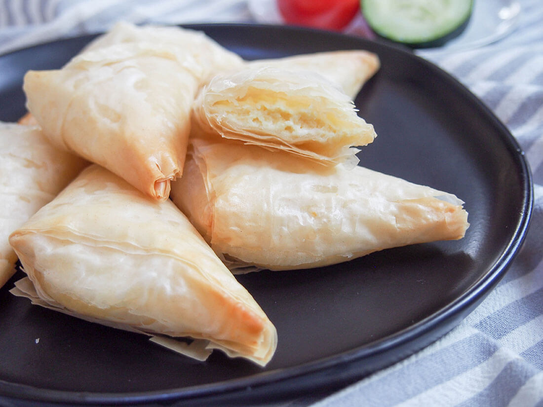 Tiropita are Greek cheese pastries combining a delicious mix of cheeses and egg wrapped in crisp filo pastry. It's one deliciously addictive snack, perfect as party food or any time! tiropita Greek cheese pastries on plate with one open showing filling