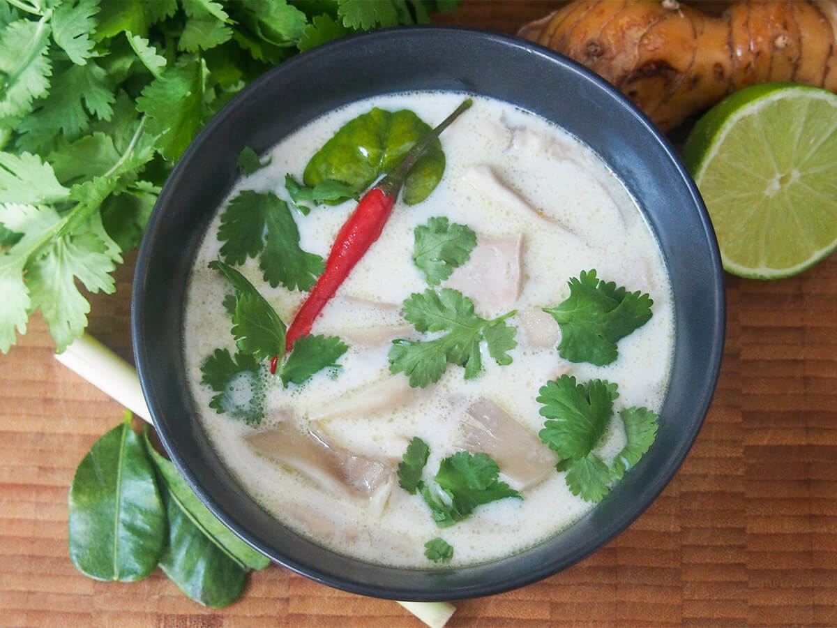 tom kha gai Thai coconut soup bowl of tom kha gai Thai soup from overhead with lime and other ingredients to side