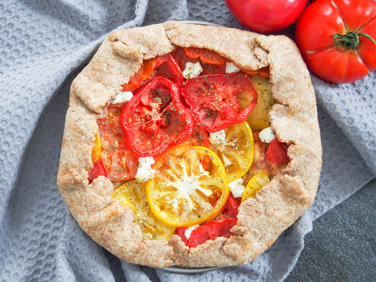 This tomato galette is an easy and delicious way to make the most of tomatoes while they are in season. You don't need too many ingredients and it's a tasty combination that's perfect for a summer lunch. whole tomato galette with tomatoes above viewed from overhead