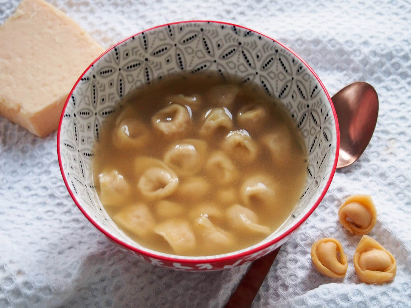Tortellini in brodo is a classic dish from the Bologna area, with small meat and cheese filled pasta cooked in homemade broth. It's comforting, packed with wonderful flavor and worth every moment of effort. bowl of tortellini in brodo with spoon and additional tortellini to side