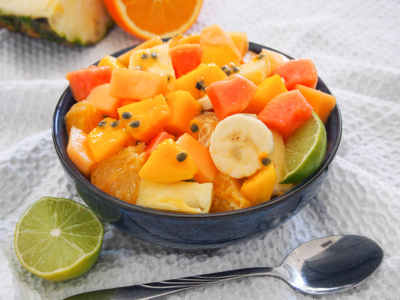 This tropical fruit salad is an easy and delicious combination of bright and flavorful fruits. It's versatile enough to be a side for a potluck, dessert or breakfast. Bowl of tropical fruit salad with cut lime to side and spoon in front