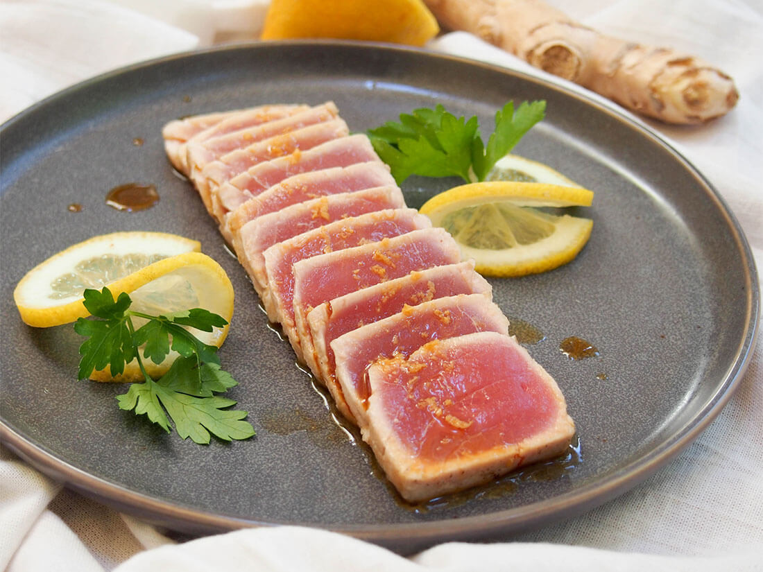 Tuna tataki is a simple Japanese dish that combines delicate, gently-seared tuna with a citrus-soy sauce given a gentle ginger kick. It's easy to make and makes a great appetizer or component to a light bento box-style meal. tuna tataki on plate with lemon and parsley as decoration