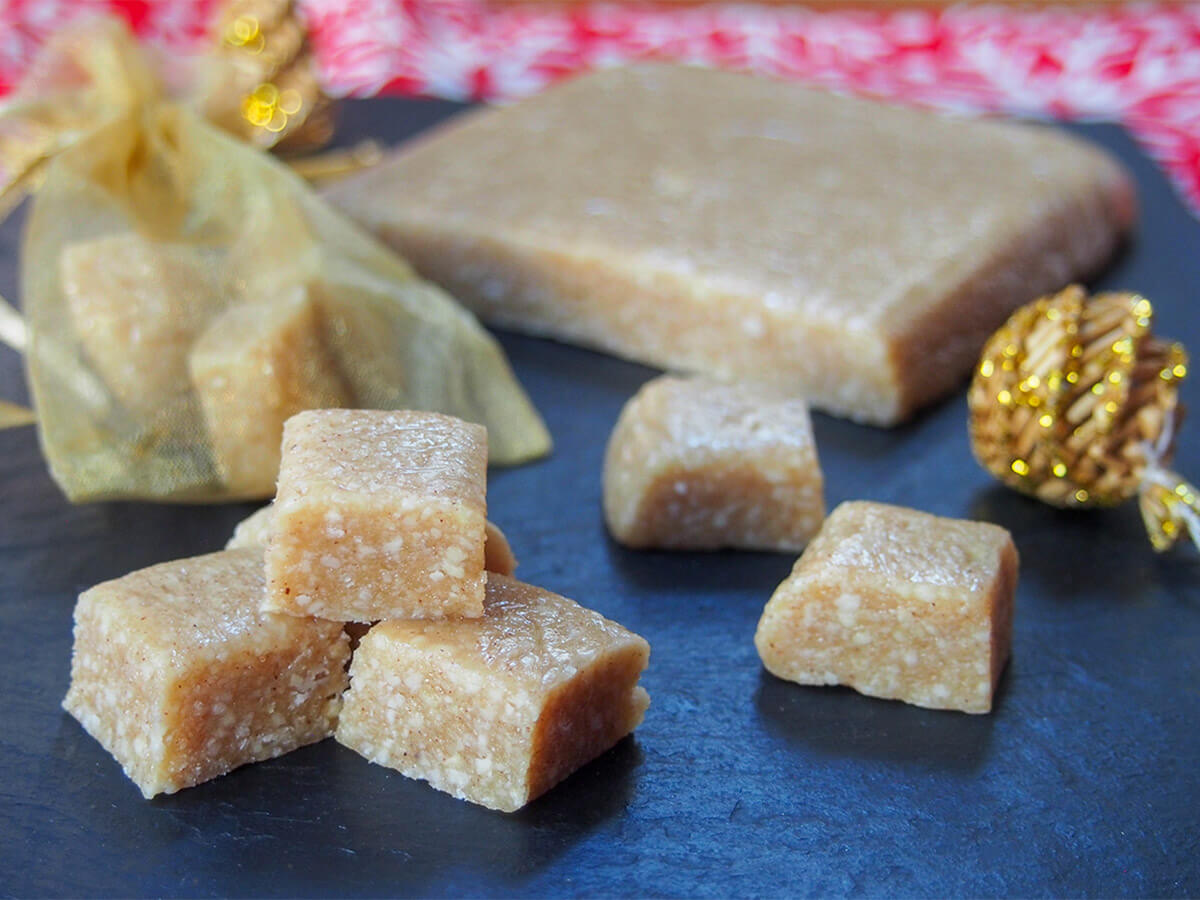 Turron de Jijona is Spanish soft nougat, full of delicious almond and honey flavor. Easy to make it's a great Holiday food gift or serve it to guests as an after dinner treat. small stach of cubes of turron de Jijona with more to side and block behind