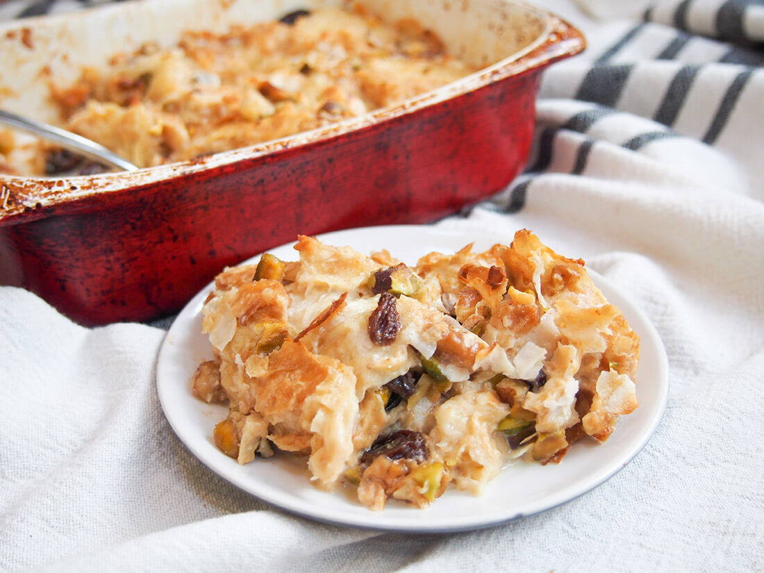Umm Ali might be relatively unknown elsewhere, but it's one of Egypt's favorite desserts. It's easy to make and is very much like a bread pudding with nuts and raisins mingled in - so delicious! umm Ali Egyptian bread pudding served on plate in front of baking dish