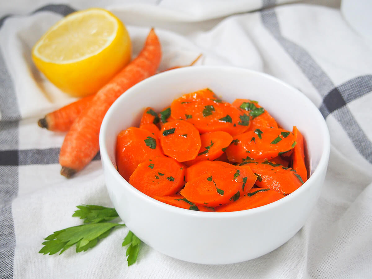 Vichy carrots (French glazed carrots) side view of bowl of vichy carrots on white cloth.