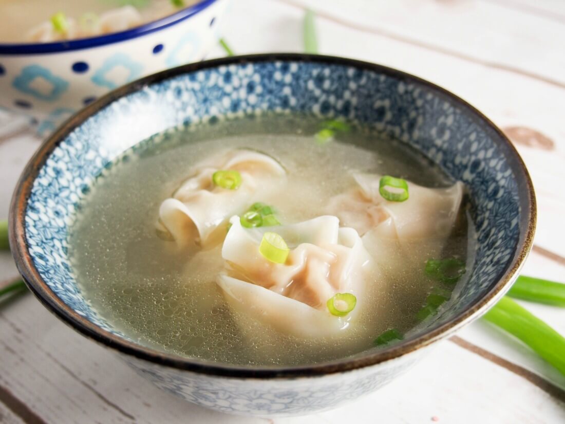Wonton soup really is so much better when you make it yourself and this recipe is so easy. Plus make extra wonton to freeze for next time. Such comfort food. bowl of wonton soup from side with corner of other bowl behind