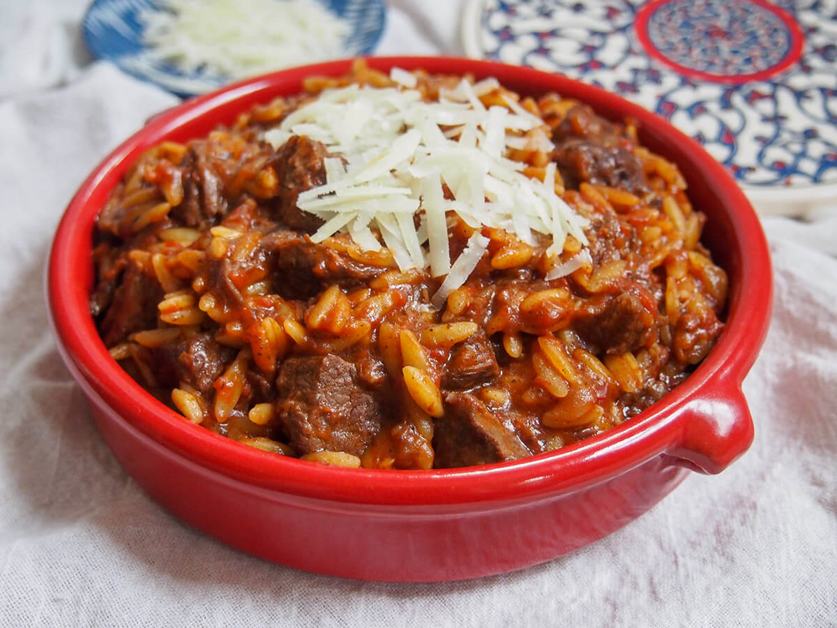 Youvetsi is a delicious Greek stew made with beef or lamb and orzo cooked in a tasty tomato-based sauce. It's flavorful, comforting and easy to make too. terracotta dish filled with youvetsi and topped with a little cheese