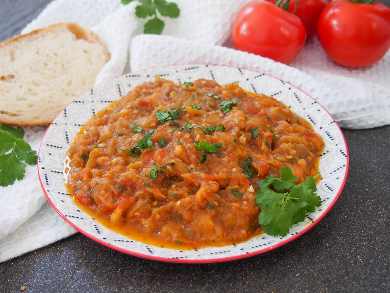 Zaalouk is a simple Moroccan salad made with eggplant, tomato, simple spices and olive oil. You can make it chunky or smooth, use it as a dip, side or spread on bread. Whichever way, it's easy and delicious. Zaalouk (Moroccan eggplant salad) on plate with bread to side