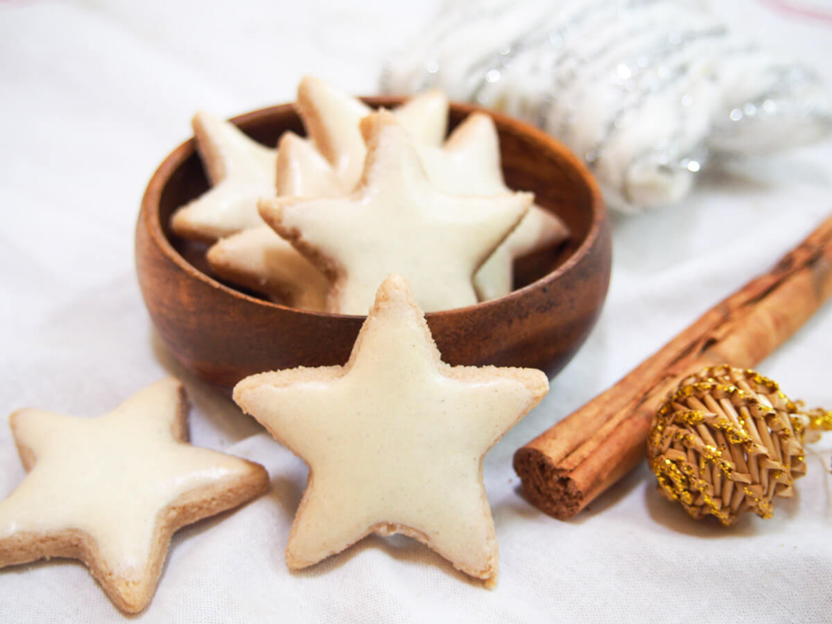 Zimtsterne are delicious cinnamon flavored nut cookies, cut and decorated into pretty stars. These cinnamon star cookies are a classic in Germany and easy to make at home with only a handful of ingredients. zimtsterne cinnamon star cookies in bowl with one standing in front and cinnamon stick to side