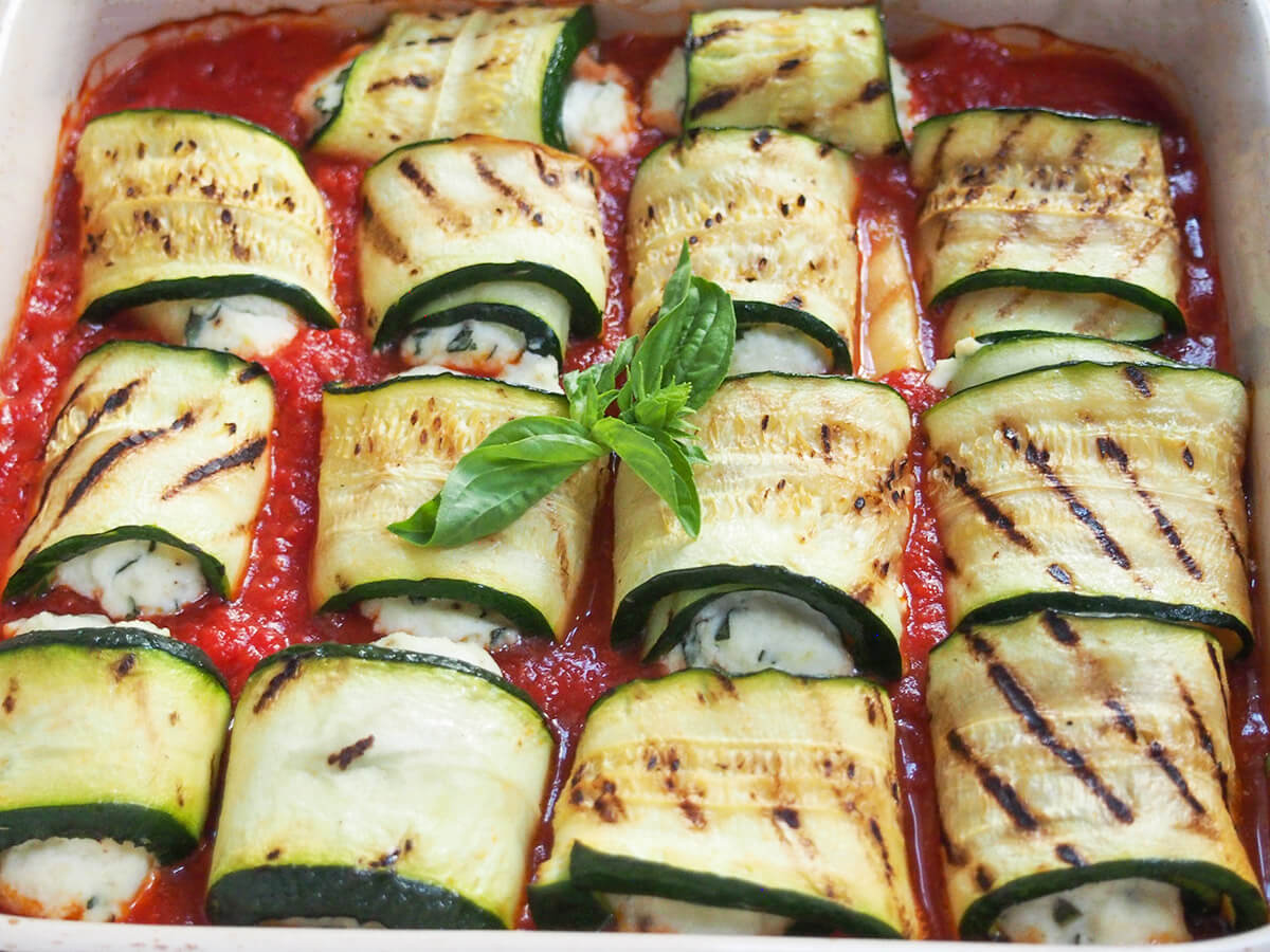 These zucchini involtini are a delicious combination of grilled zucchini wrapped around a basil and lemon seasoned ricotta filling, nestled in marinara sauce. It's surprisingly light, comforting and incredibly tasty. side view of dish of zucchini involtini